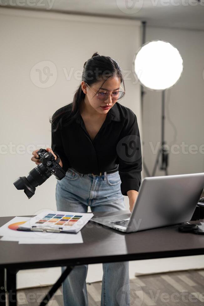 ein Fachmann asiatisch weiblich Fotograf ist Überprüfung Bilder auf ihr Laptop, Arbeiten im ein Studio. foto