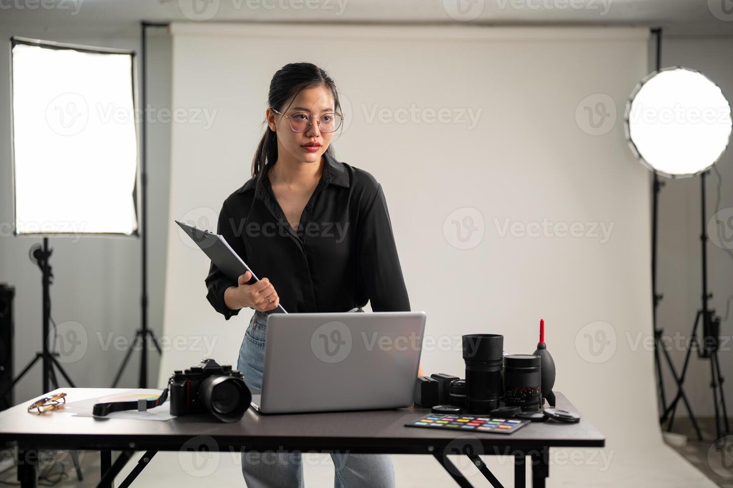 ein elegant asiatisch weiblich Fotograf im ein schwarz Hemd ist Stehen im ihr Fotoshooting Studio. foto