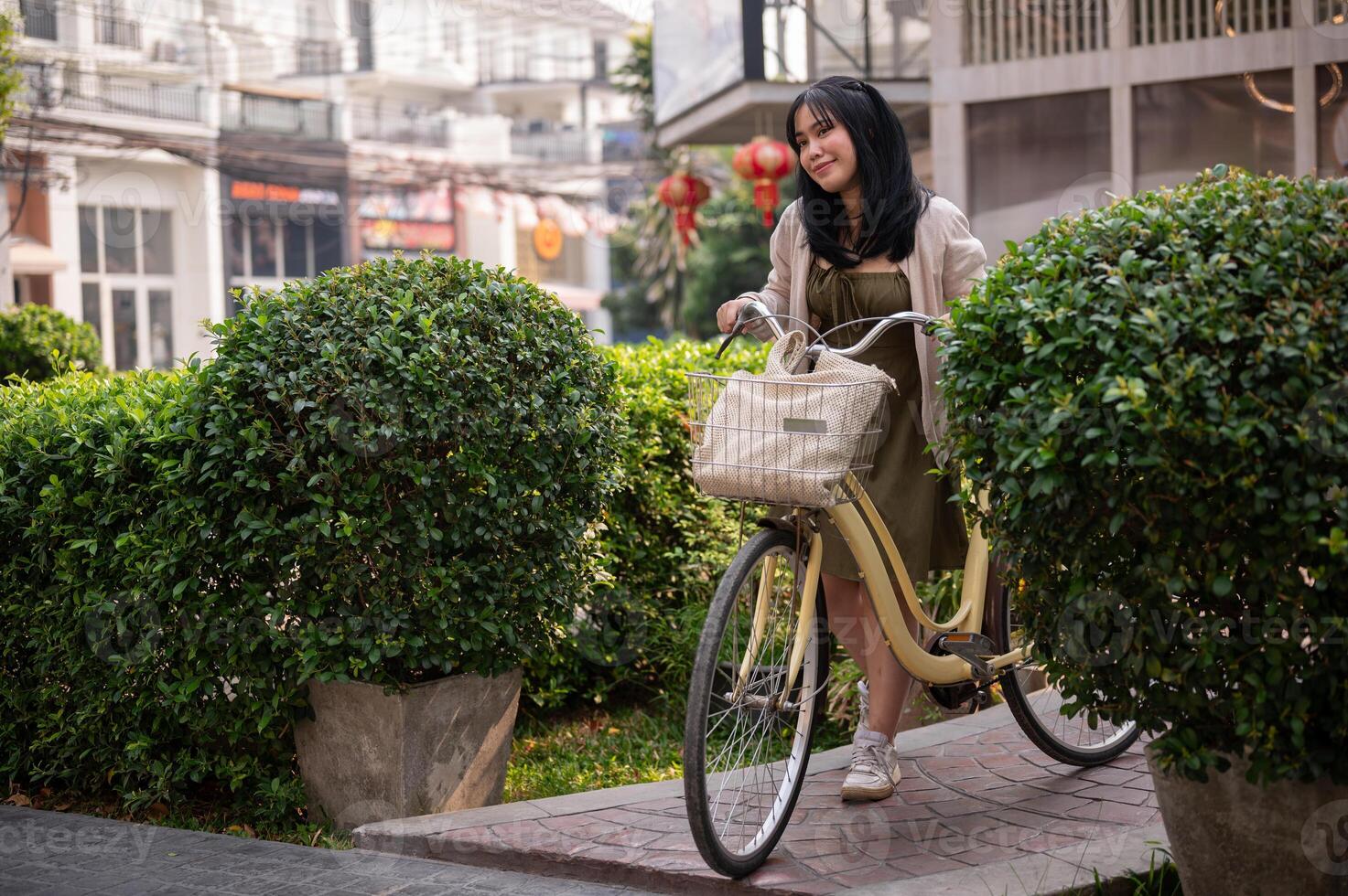 ein Glücklich, schön jung asiatisch Frau ist schieben ihr Fahrrad auf ein Fußweg im das Stadt. foto