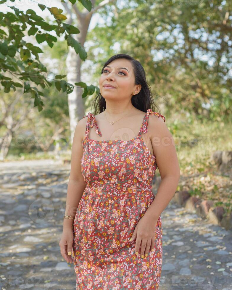 Frau tragen Kleid mit Blumen bewundern Natur im ein Öffentlichkeit Park. sonnig Sommer- Tag. foto