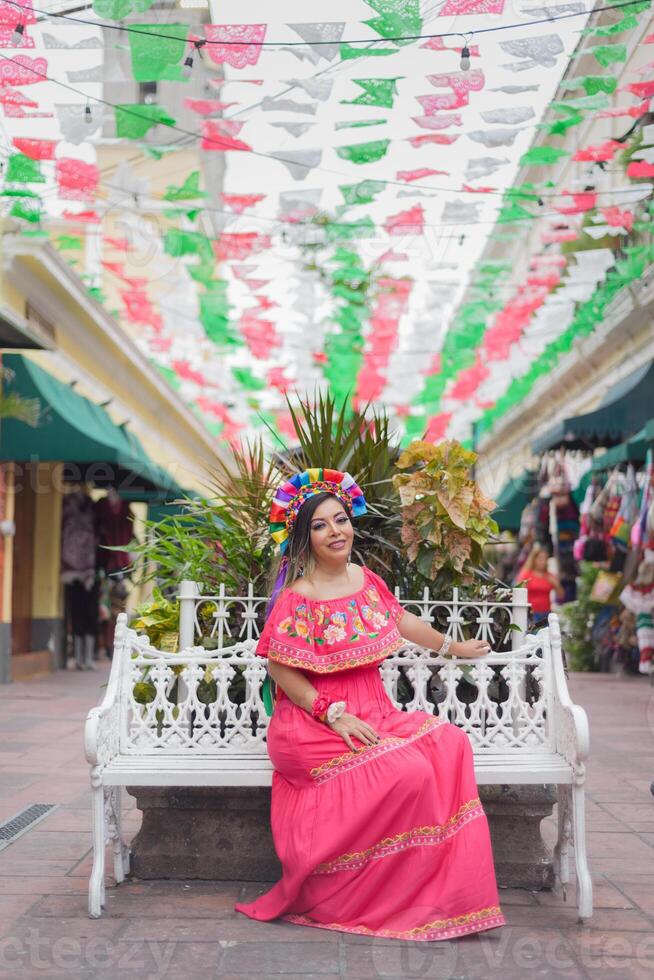 Mexikaner Frau sitzend tragen traditionell Kleid. Straße dekoriert mit Farben von das Mexikaner Flagge. cinco de Mayo Feier. foto