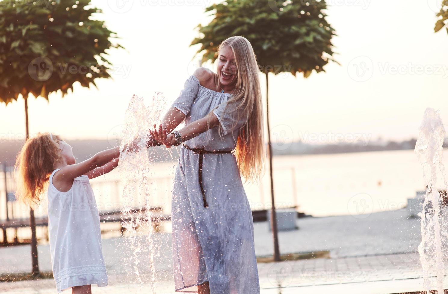 heiße Atmosphäre. An einem heißen sonnigen Tag beschließen Mutter und ihre Tochter, den Brunnen zur Abkühlung zu benutzen und Spaß damit zu haben foto