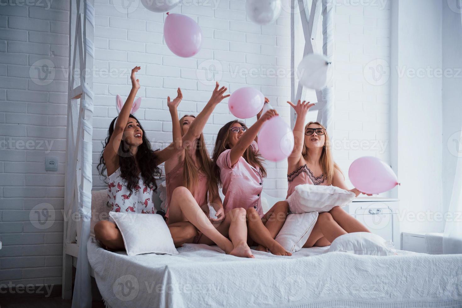 wie Kinder auf der Party. auf dem weißen Luxusbett mit Luftballons und Hasenohren sitzen. Vorstellung von Bachelorette foto