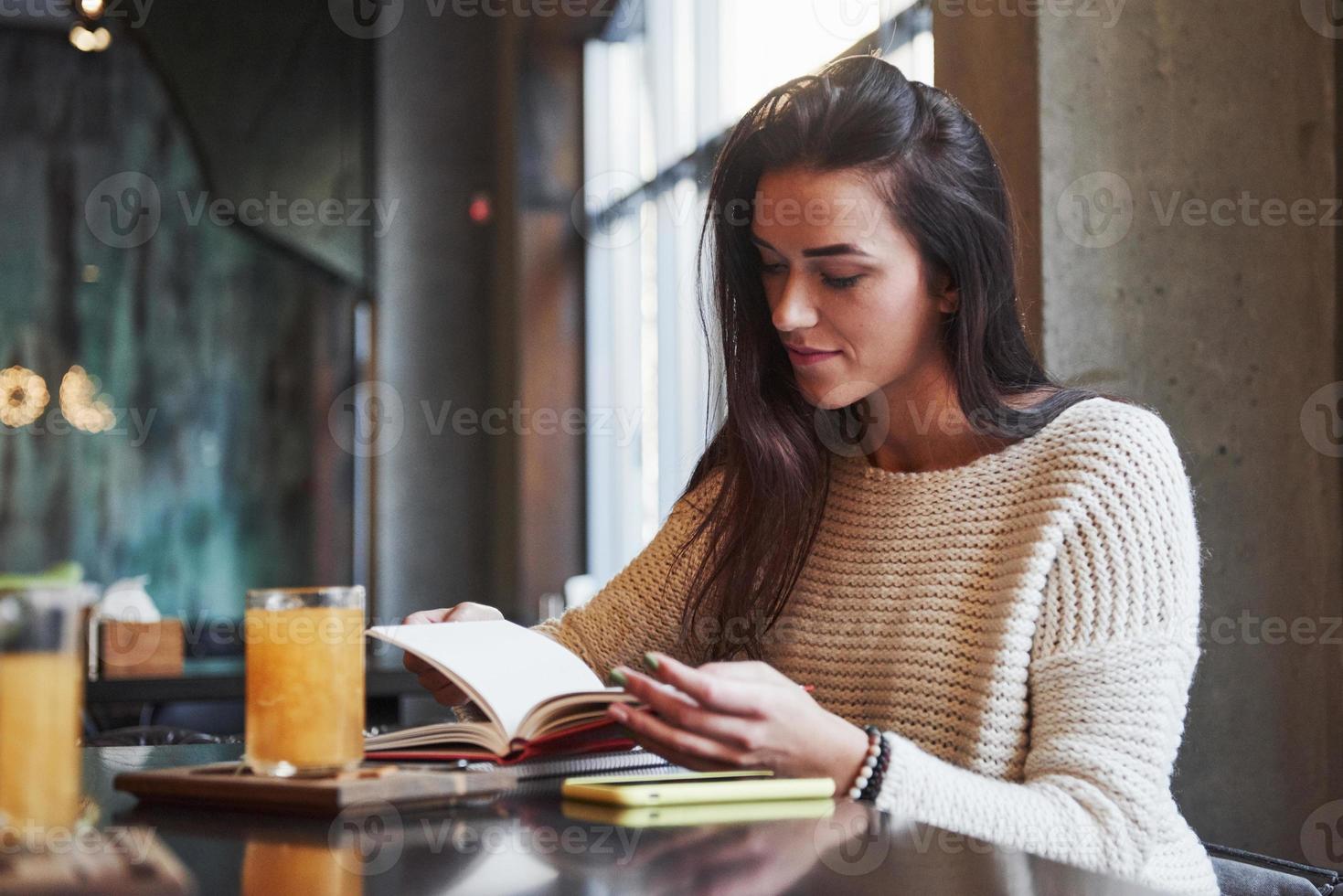 Zeit zum Lesen und Erhalten neuer interessanter Informationen, während Sie im Restaurant mit Tisch und gelbem Getränk darauf sitzen foto