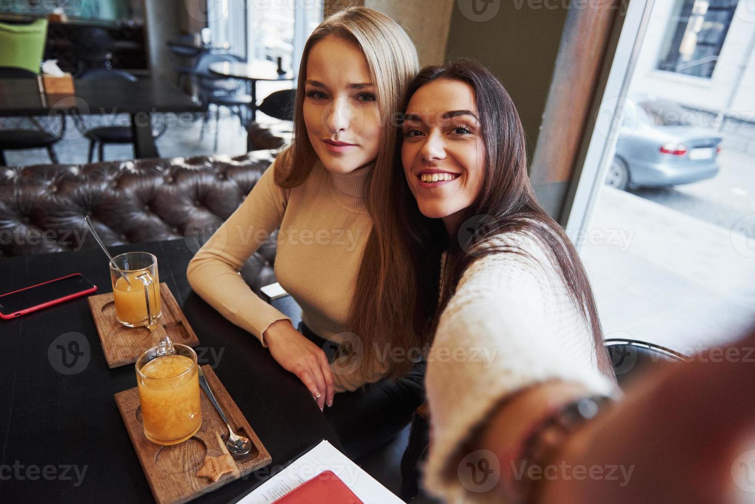 Foto vom Handy des Mädchens. Junge Freundinnen machen Selfie im Restaurant mit zwei gelben Getränken auf dem Tisch