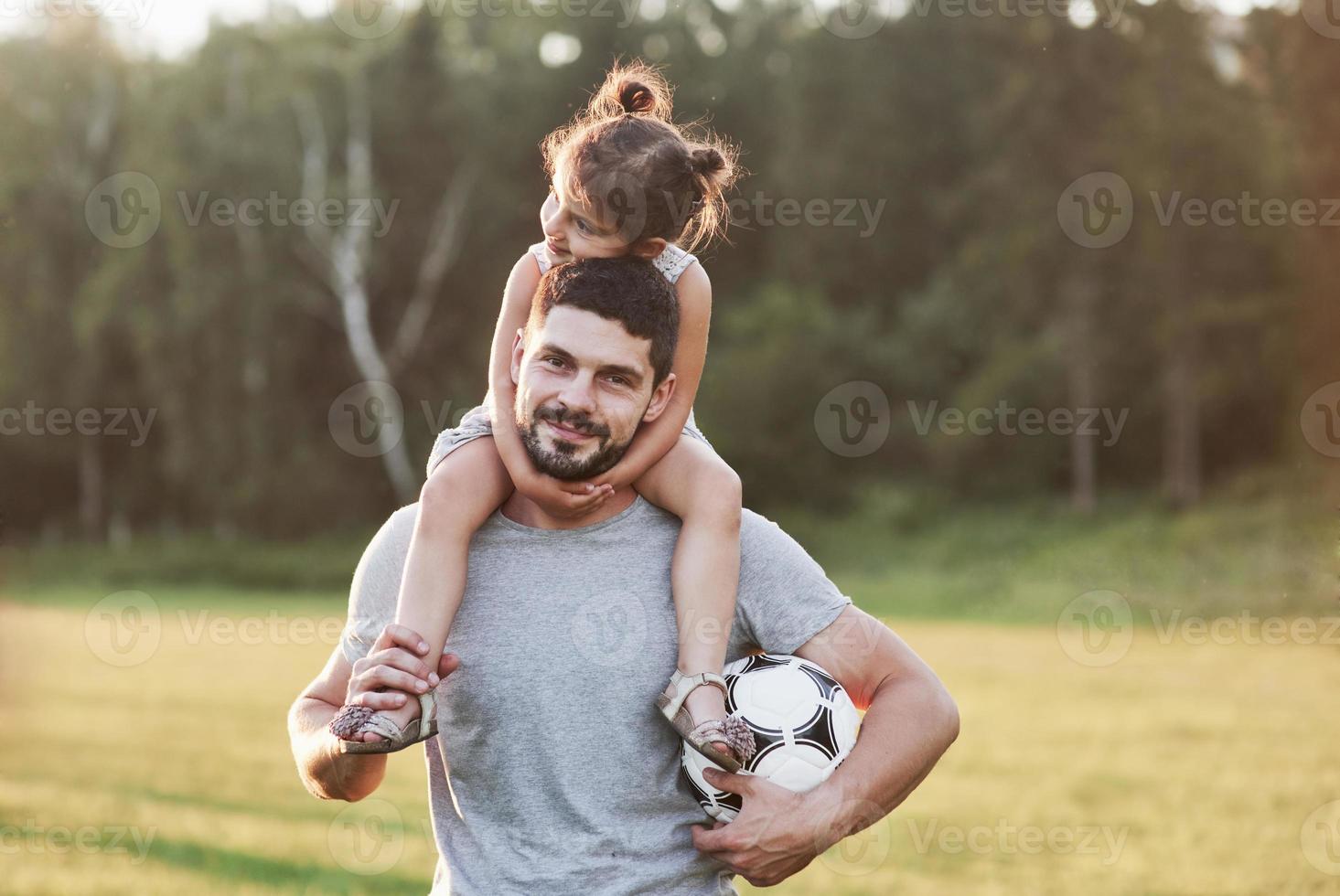 was für ein schönes Wetter heute ist. Foto von Papa mit seiner Tochter bei schönem Gras und Wald im Hintergrund