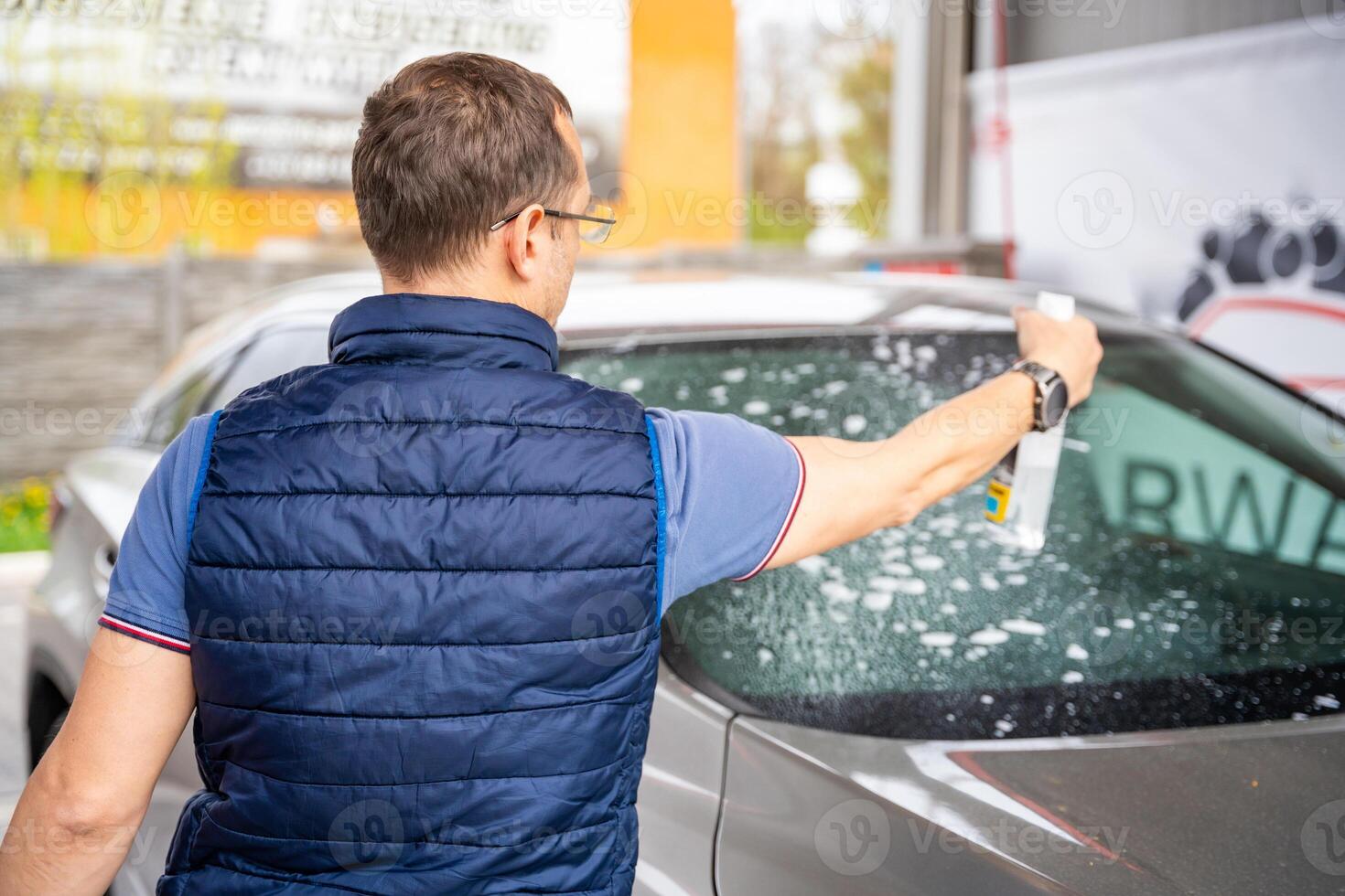 jung Mann gilt Flüssigkeit zu sauber Fenster von das Auto im Selbstbedienung Auto waschen. hoch Qualität Foto