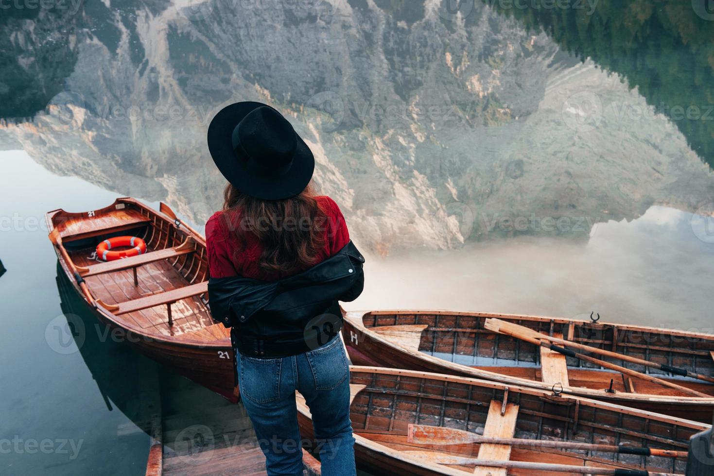 Spiegelungen im Wasser sehen aus wie echte. Frau mit schwarzem Hut genießt majestätische Berglandschaft in der Nähe des Sees mit Booten foto