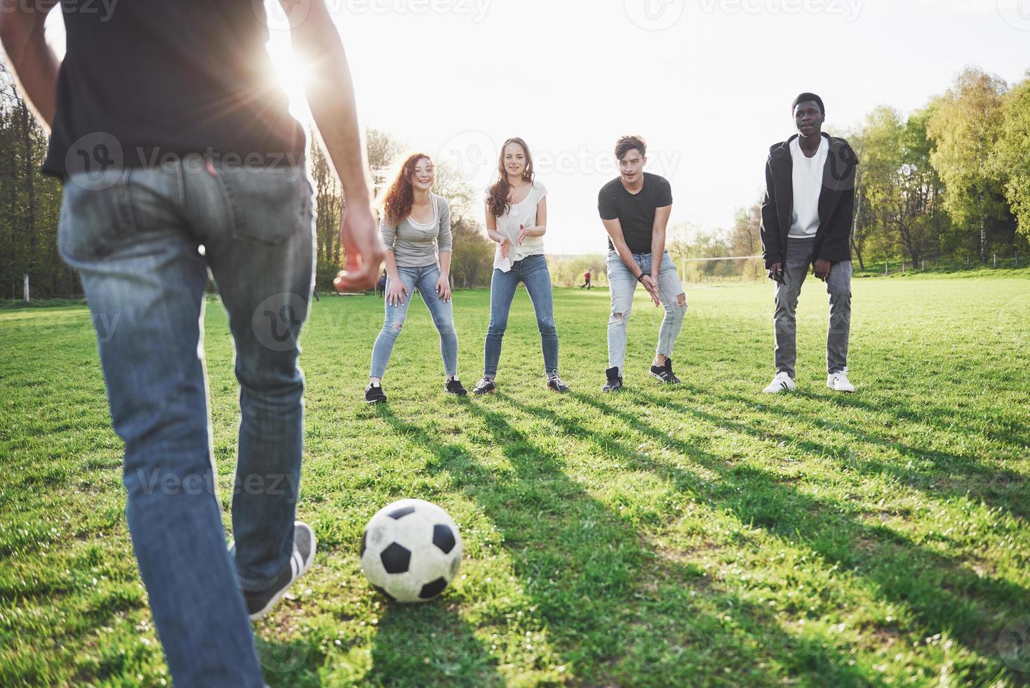 eine Gruppe von Freunden in legerem Outfit spielt Fußball unter freiem Himmel. Leute haben Spaß und haben Spaß. aktive Erholung und malerischer Sonnenuntergang foto