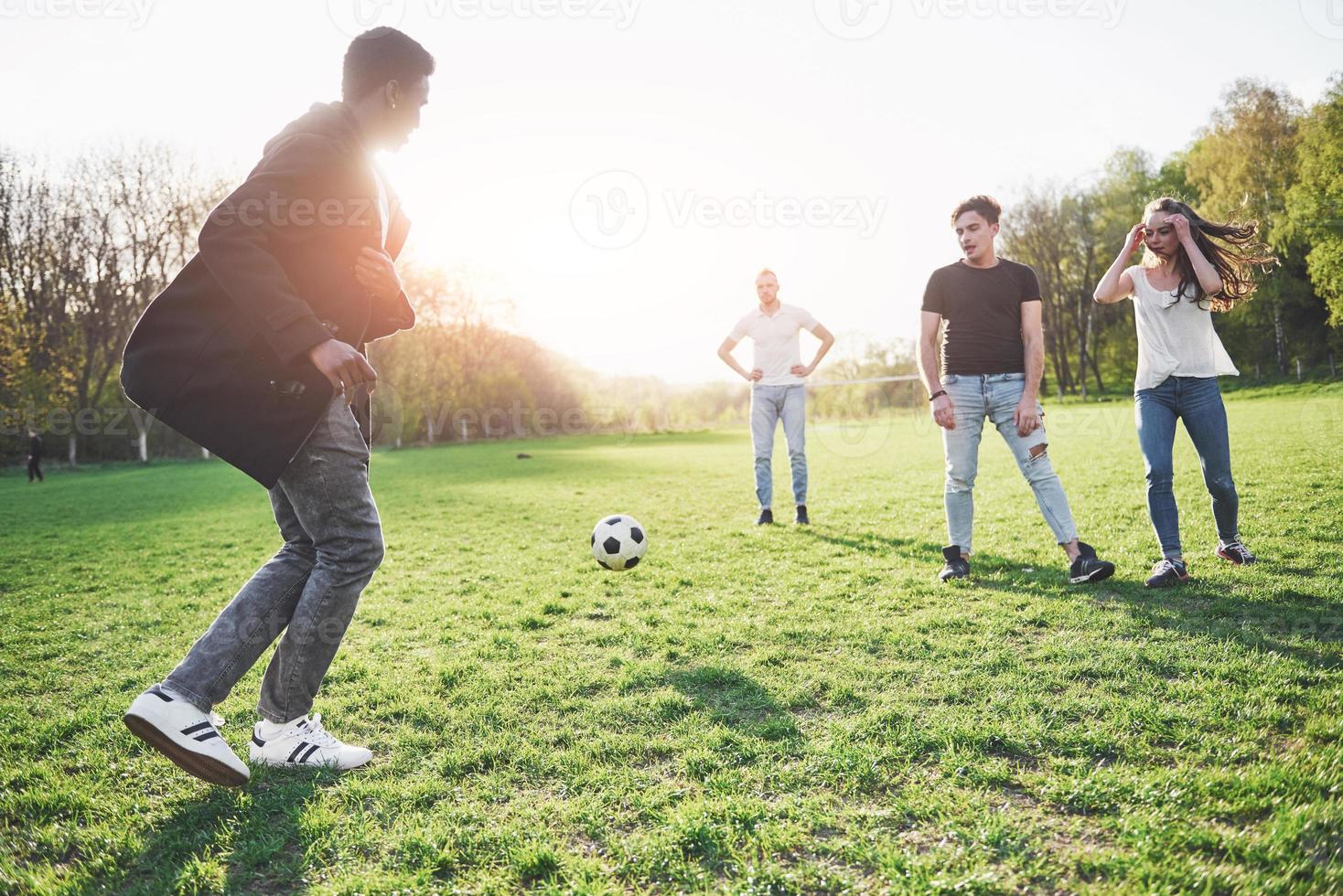 eine Gruppe von Freunden in legerem Outfit spielt Fußball unter freiem Himmel. Leute haben Spaß und haben Spaß. aktive Erholung und malerischer Sonnenuntergang foto