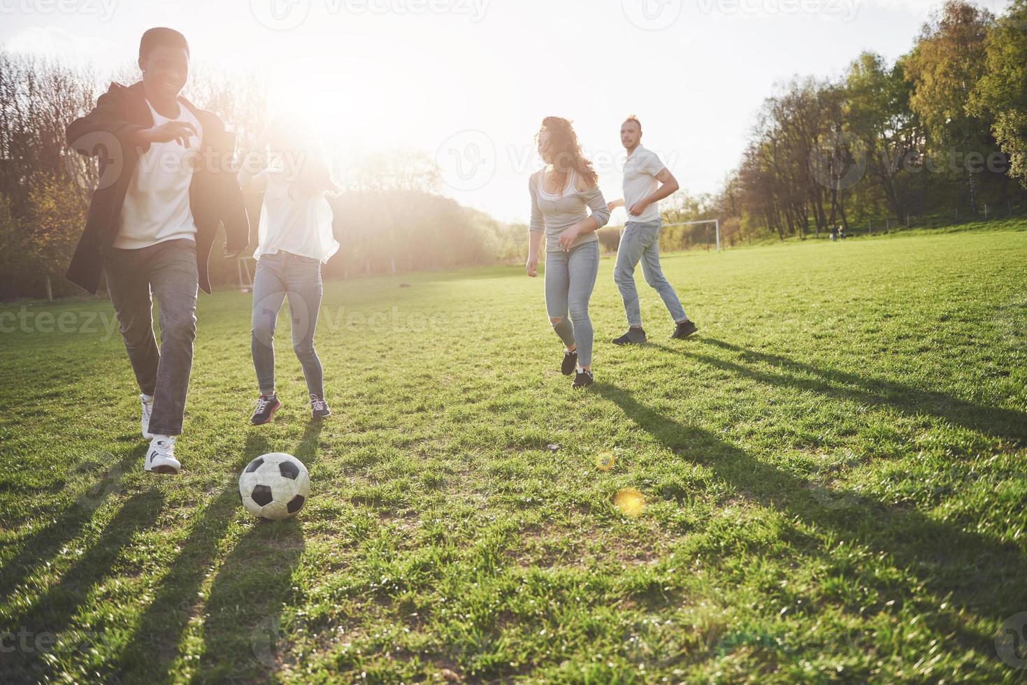 eine Gruppe von Freunden in legerem Outfit spielt Fußball unter freiem Himmel. Leute haben Spaß und haben Spaß. aktive Erholung und malerischer Sonnenuntergang foto