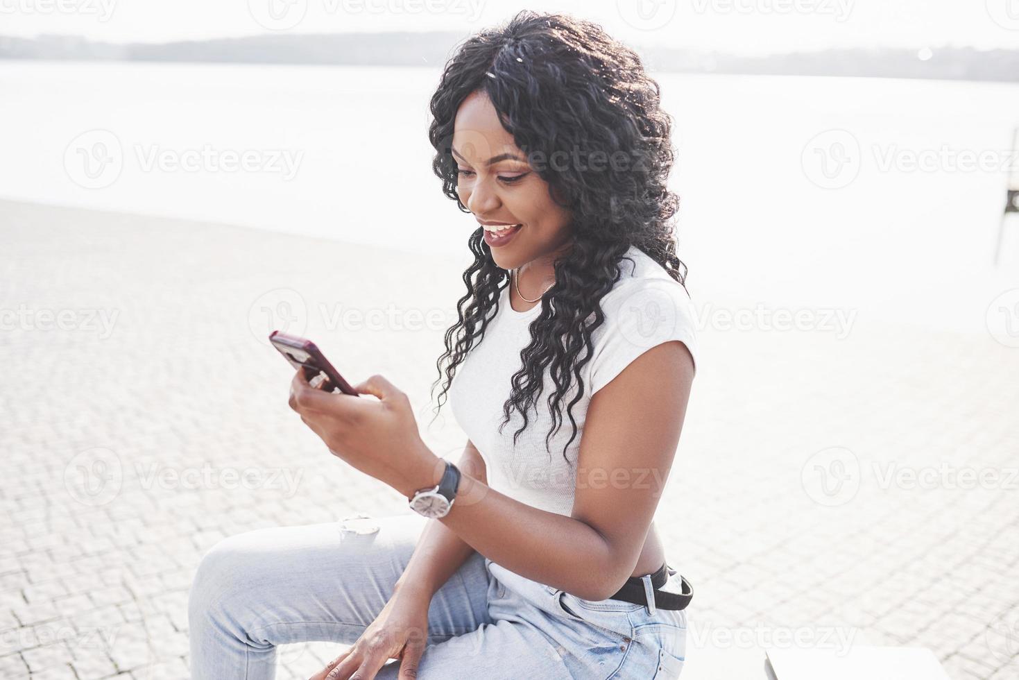 lächelndes schwarzes Mädchen mit einem Telefon am Wasser foto