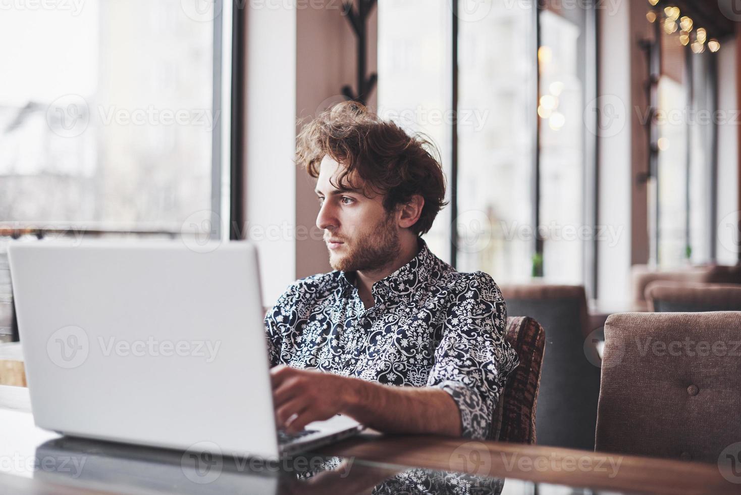 Junger gutaussehender Mann, der mit einer Tasse Kaffee im Büro sitzt und an einem Projekt arbeitet, das mit modernen Cyber-Technologien verbunden ist. Geschäftsmann mit Notebook, der versucht, die Frist im Bereich des digitalen Marketings einzuhalten? foto