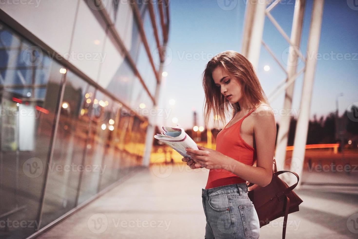 Ein junges schönes Mädchen mit einem Rucksack hinter den Schultern, das auf der Straße in der Nähe eines Flughafens steht. sie ist gerade vom rest angekommen und sehr glücklich foto