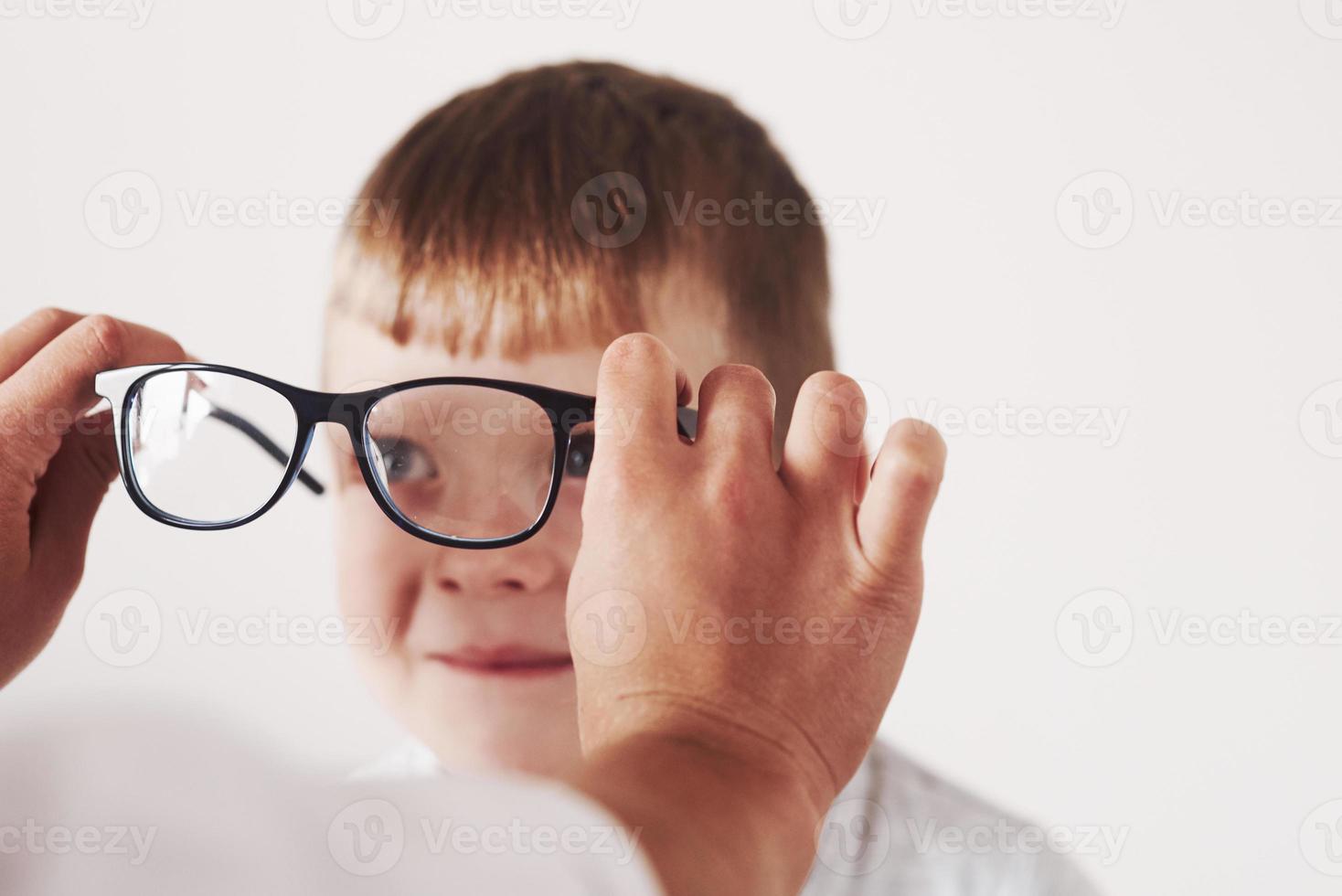 lächelt und sieht die Frau an. Arzt gibt dem Kind eine neue schwarze Brille für seine Vision foto