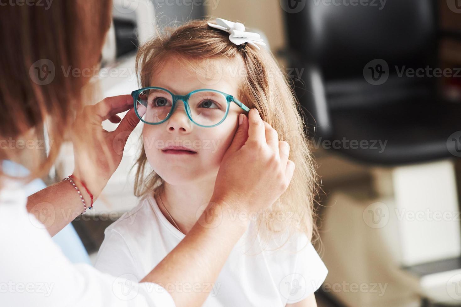 sitzt gut bei dir. Arzt gibt dem Kind eine neue Brille für seine Sehkraft foto