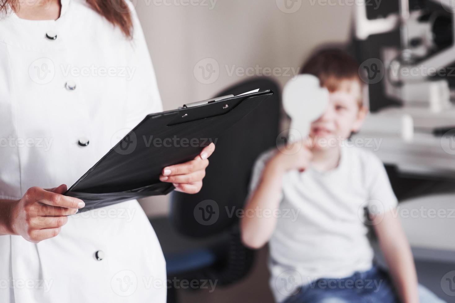 Frau mit Dokumenten testet die Sehschärfe eines kleinen Jungen foto