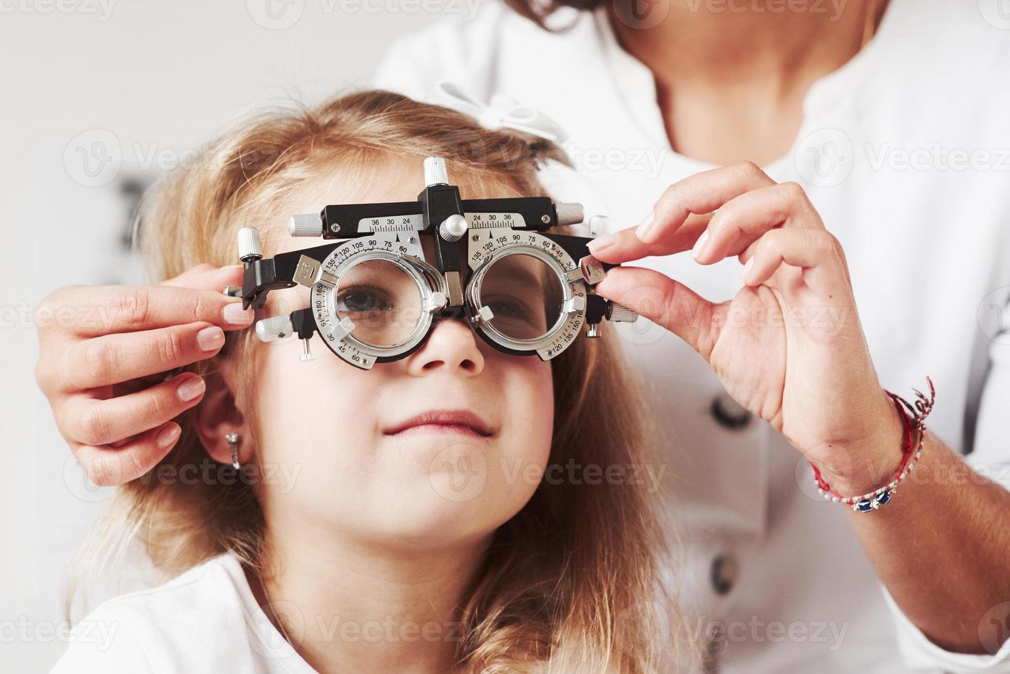 schwer, dieses Wort zu verstehen. Arzt, der die Sicht des kleinen Mädchens überprüft und den Phoropter einstellt foto