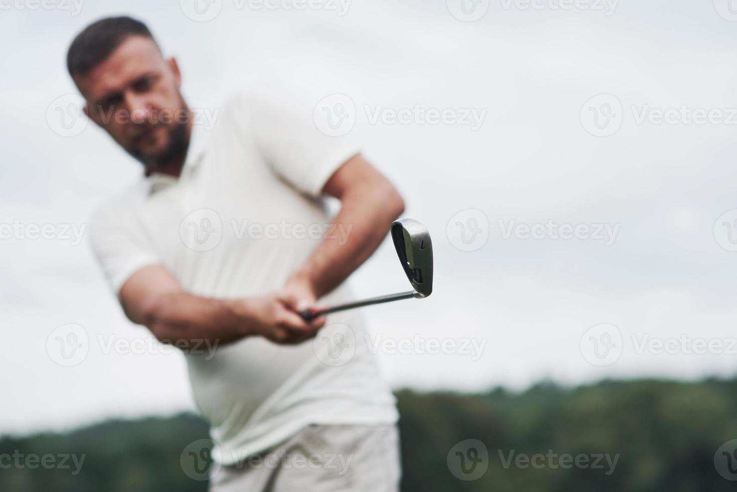 fokussiert auf die Endseite eines Sticks. Porträt des Golfspielers im Rasen und Ausrüstung in der Hand foto
