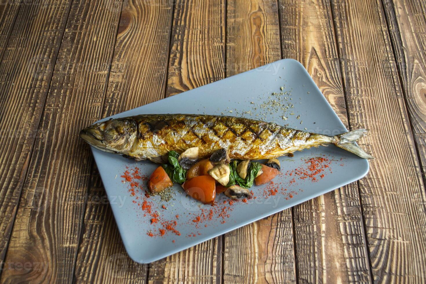 gegrillt Fisch mit Gemüse im ein Teller auf ein hölzern Tisch. foto