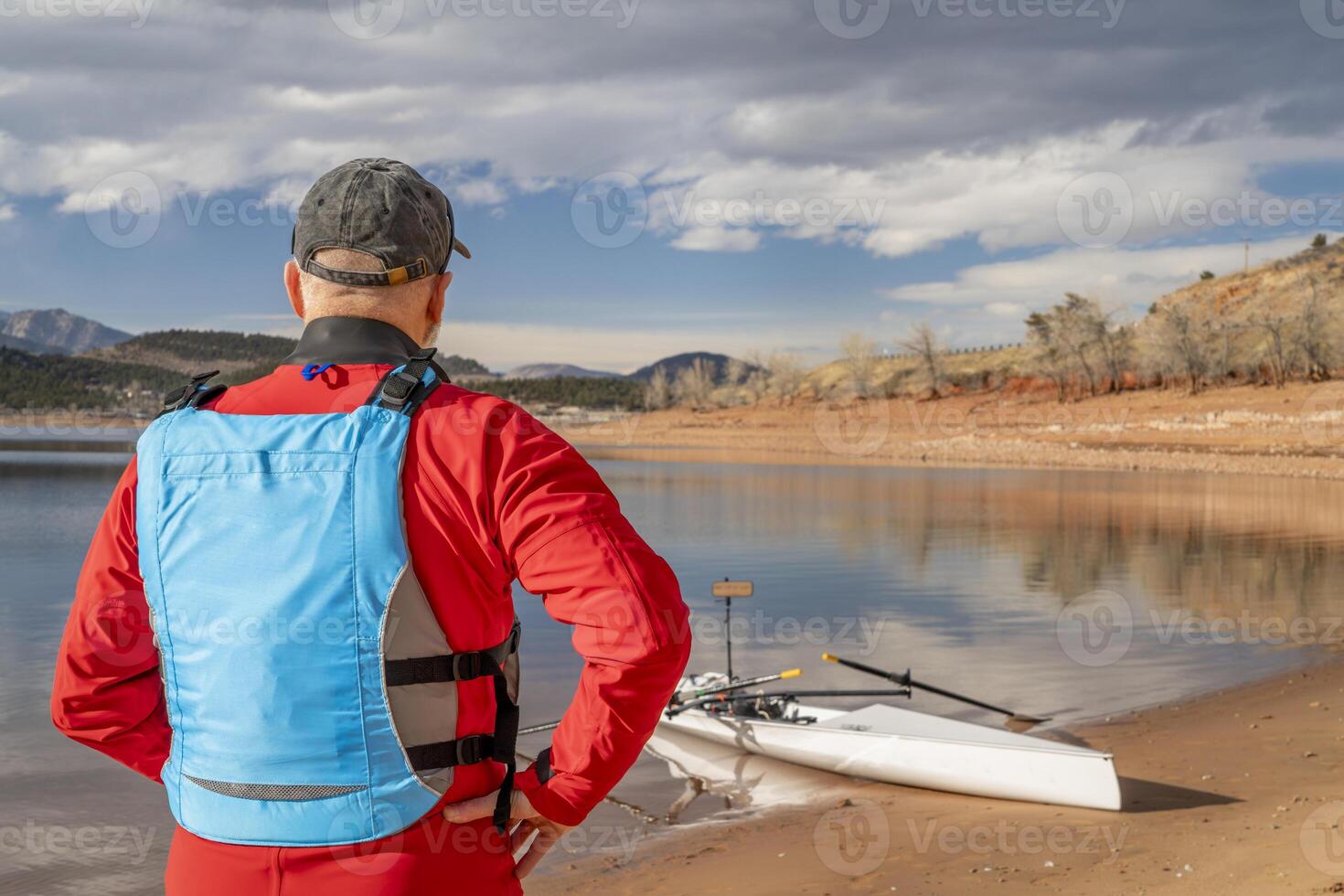 Senior Mann tragen Trockenanzug und Leben Jacke mit ein Rudern Schale auf See Ufer, Winter im Nord Colorado foto