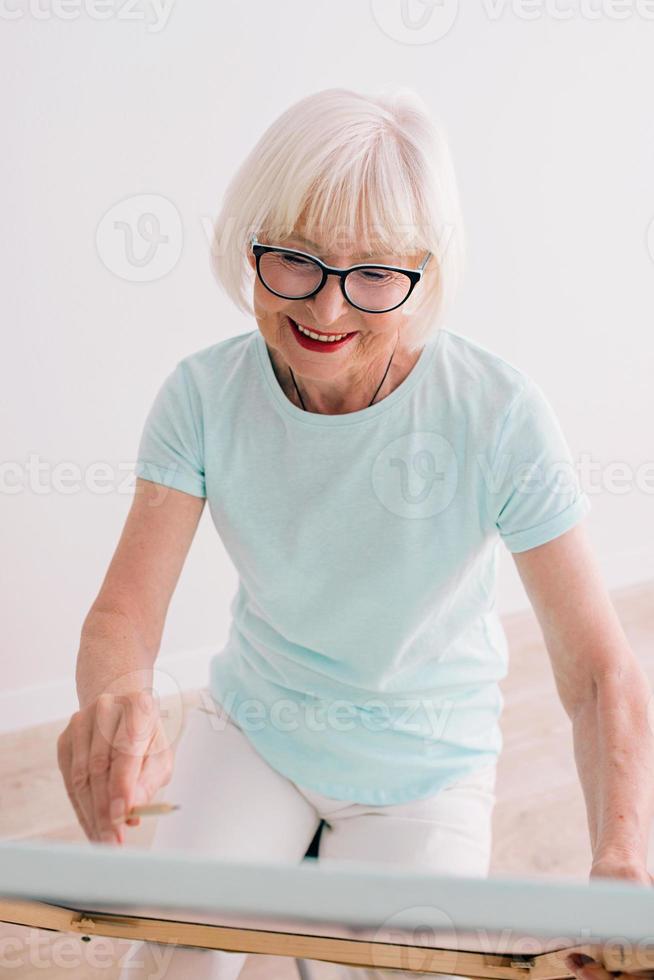 Senior fröhliche Künstlerin in Brille mit grauer Haarzeichnung. Kreativität, Kunst, Hobby, Berufskonzept foto