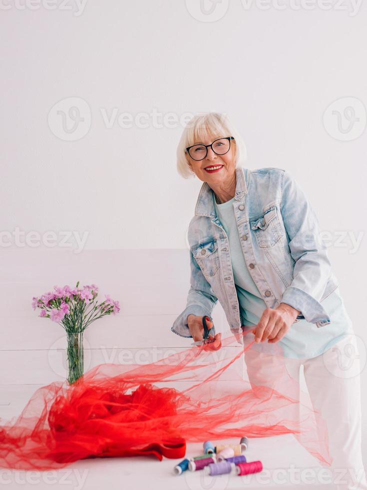 Senior Rentner fröhliche stilvolle Frau Kleidung Designer in Jeansjacke bei der Arbeit. Handarbeit, Mode, Hobby, Design, Alterskonzept foto