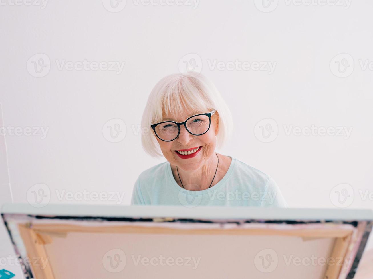 Senior fröhliche Künstlerin in Gläsern mit grauen Haaren, die mit Bleistiftblumen in der Vase zeichnen. Kreativität, Kunst, Hobby, Berufskonzept foto