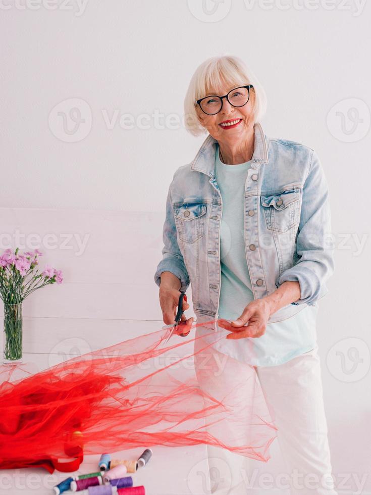 Senior Rentner fröhliche stilvolle Frau Kleidung Designer in Jeansjacke bei der Arbeit. Handarbeit, Mode, Hobby, Design, Alterskonzept foto