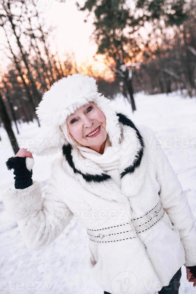 ältere Frau in weißem Hut und Pelzmantel, die den Winter im Schneewald genießt. Winter, Alter, Saisonkonzept foto
