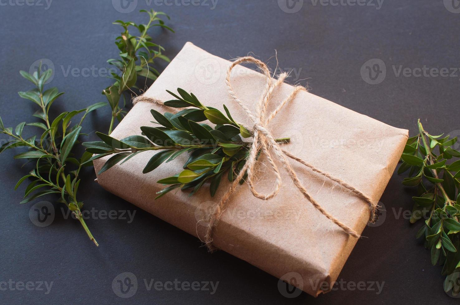 Bastelgeschenkbox mit Knoten natur mit grünen Blättern auf schwarzem Hintergrund foto