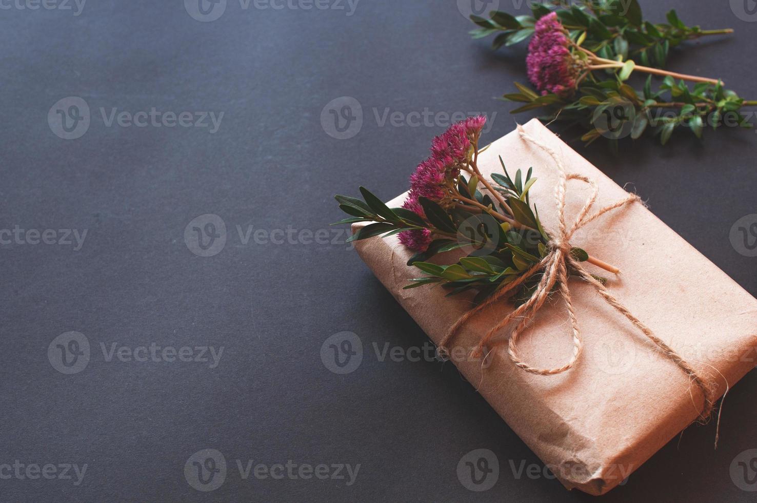 Bastelgeschenkbox mit Knoten natur mit rosa kleinen Blumen auf schwarzem Hintergrund. foto