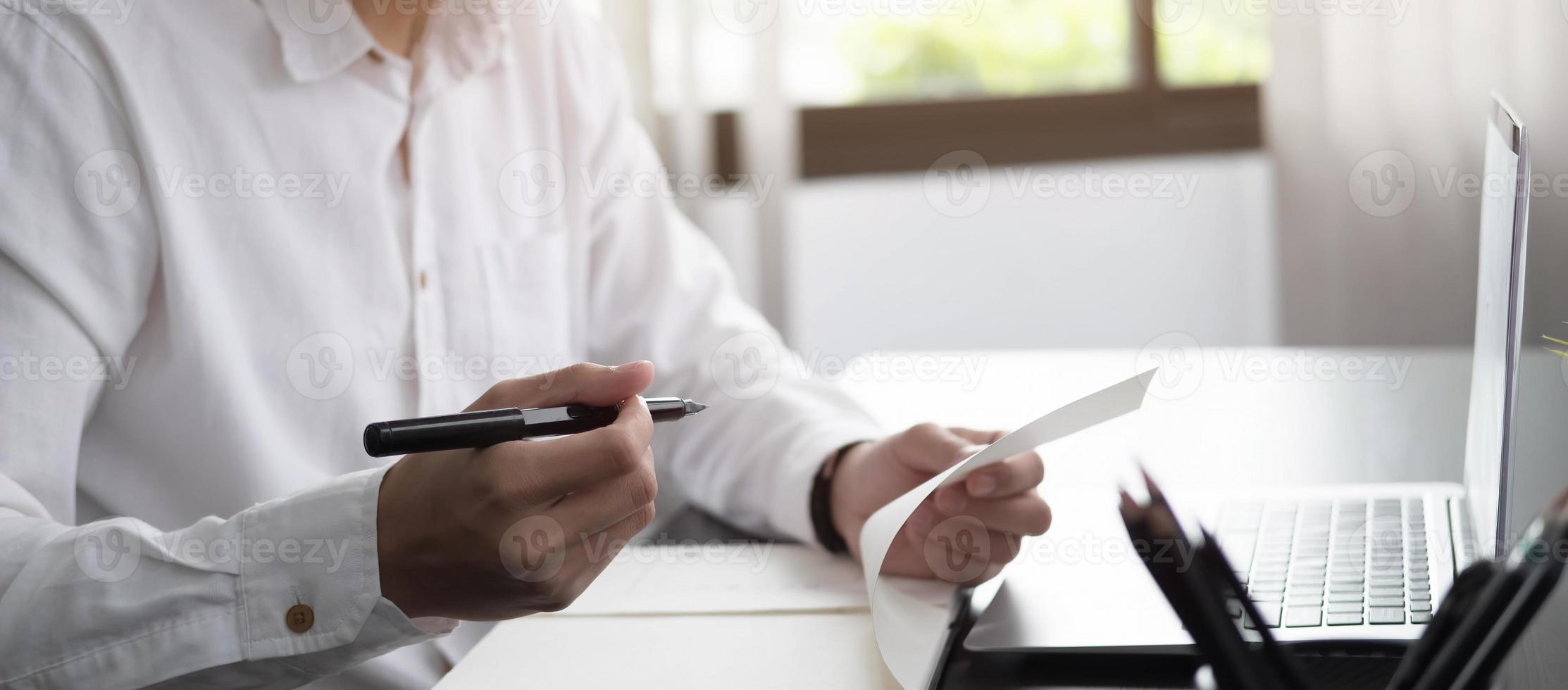 abgeschnittene Fotohand des Mannes, der eine Liste erstellt und Notizen im Notizblock macht, die zu Hause mit dem Laptop online arbeitet oder lernt foto