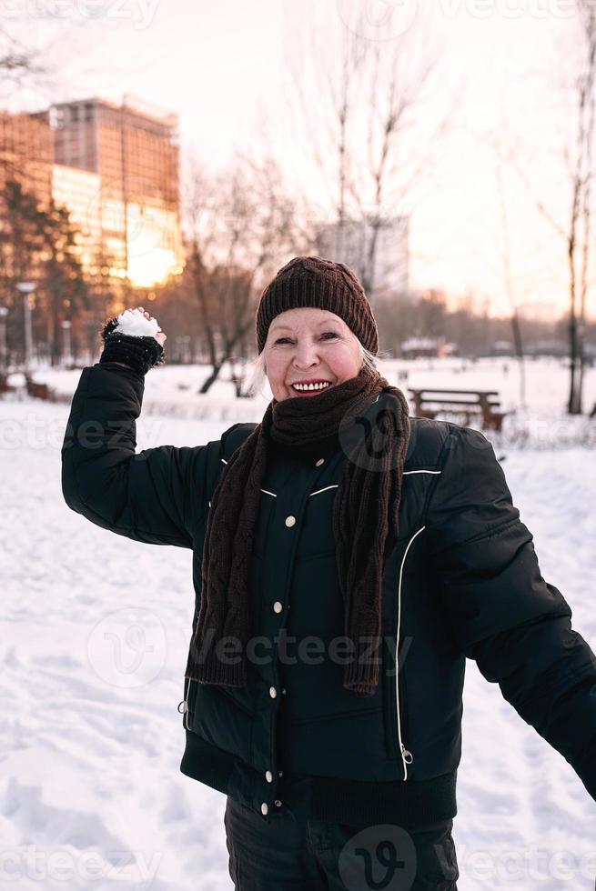 ältere Frau mit Hut und sportlicher Jacke, die im Schneewinterpark schneit. Winter, Alter, Sport, Aktivität, Saisonkonzept foto