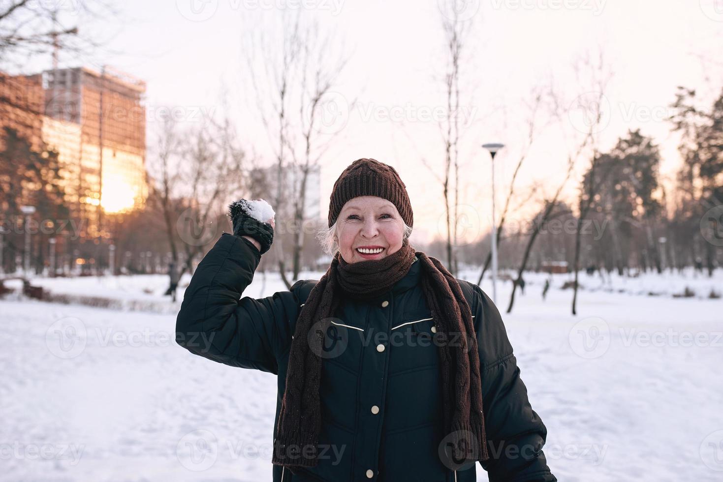 ältere Frau mit Hut und sportlicher Jacke, die im Schneewinterpark schneit. Winter, Alter, Sport, Aktivität, Saisonkonzept foto