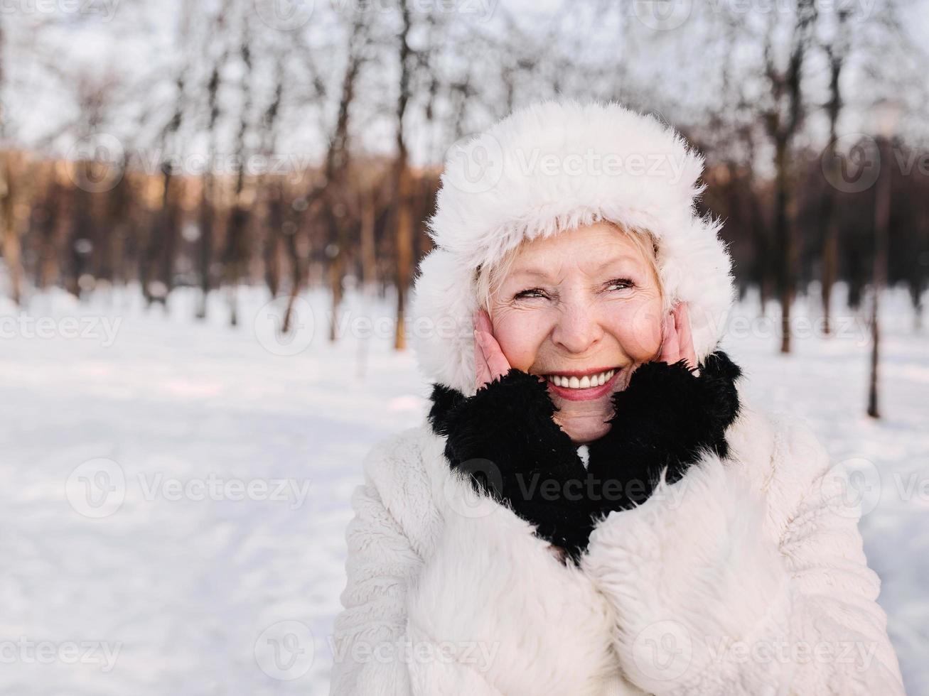 ältere Frau in weißem Hut und Pelzmantel, die den Winter im Schneewald genießt. Winter, Alter, Saisonkonzept foto