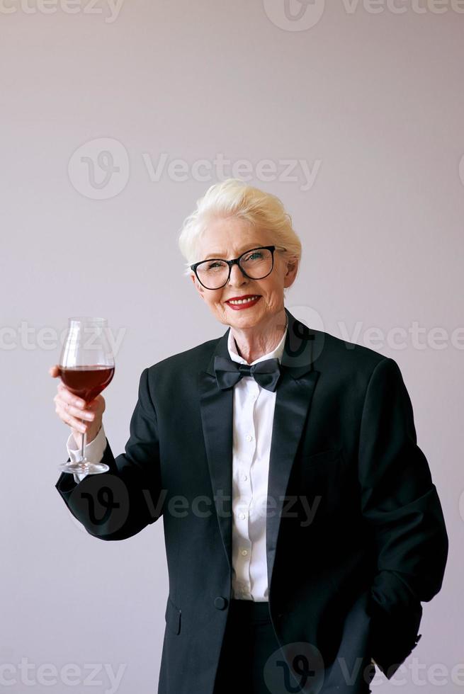 stilvolle reife Sommelier-Senior-Frau im Smoking mit einem Glas Wein. Spaß, Party, Stil, Lifestyle, Arbeit, Alkohol, Feierkonzept foto