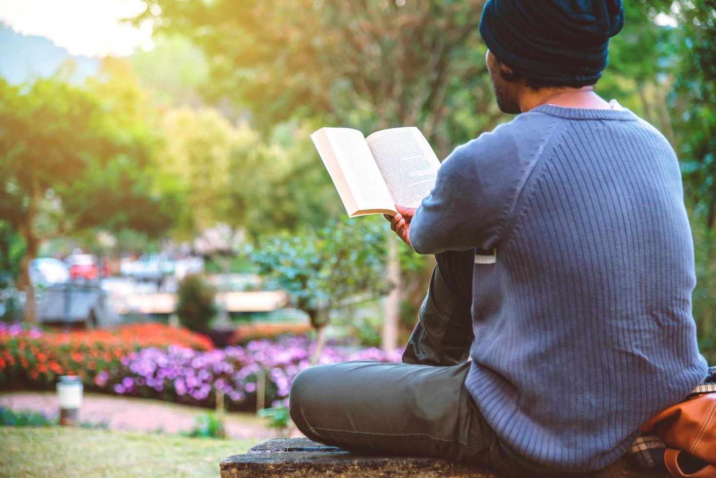 der junge mann bereist die natur am berg, sitzt und entspannt ein buch im blumengarten. foto