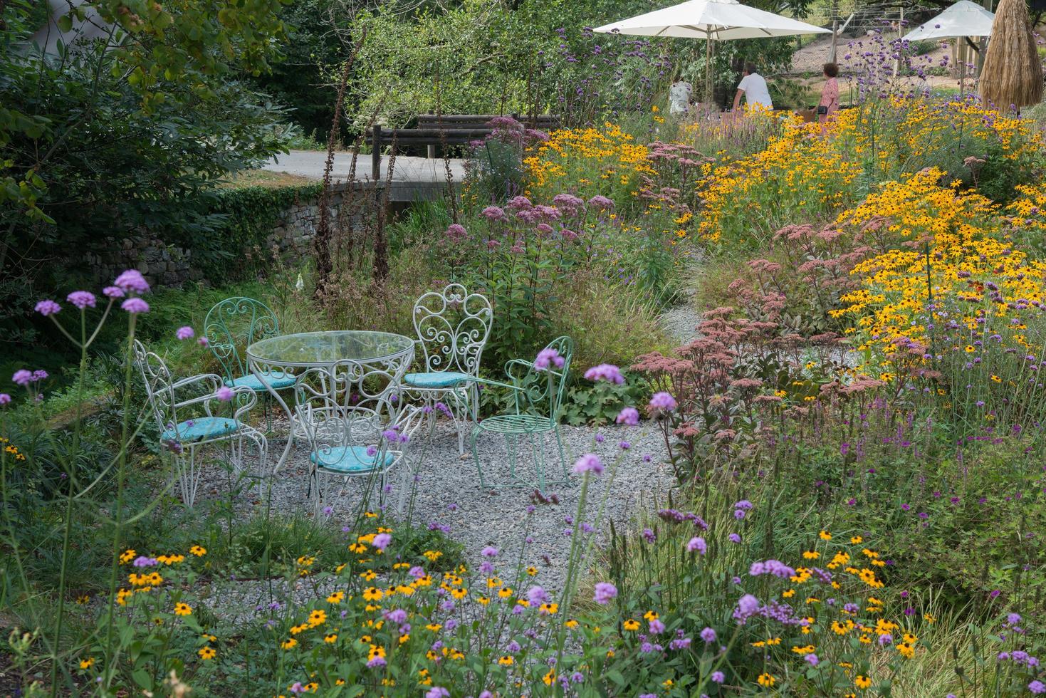 schöner Garten mit bunten Wildblumen. unbekannte Leute in der Ferne. Gartenmöbel aus Metall. foto