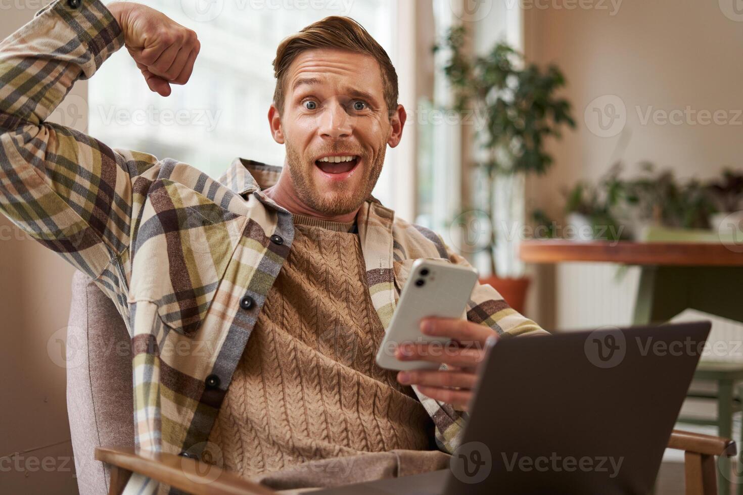 Porträt von komisch sportlich, passen Kerl im Cafe, Sitzung auf Stuhl mit Laptop und Smartphone, Biegen Bizeps, zeigen seine Muskeln auf Kamera und Prahlerei Wie stark er ist foto