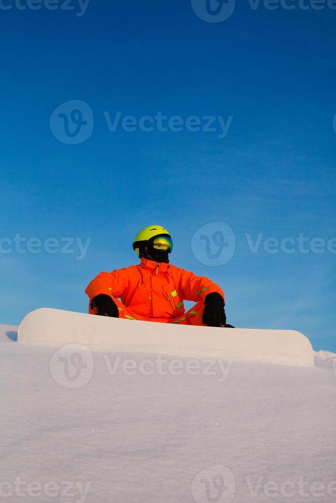 Snowboarder Freerider mit weißem Snowboard sitzt oben auf der Skipiste foto