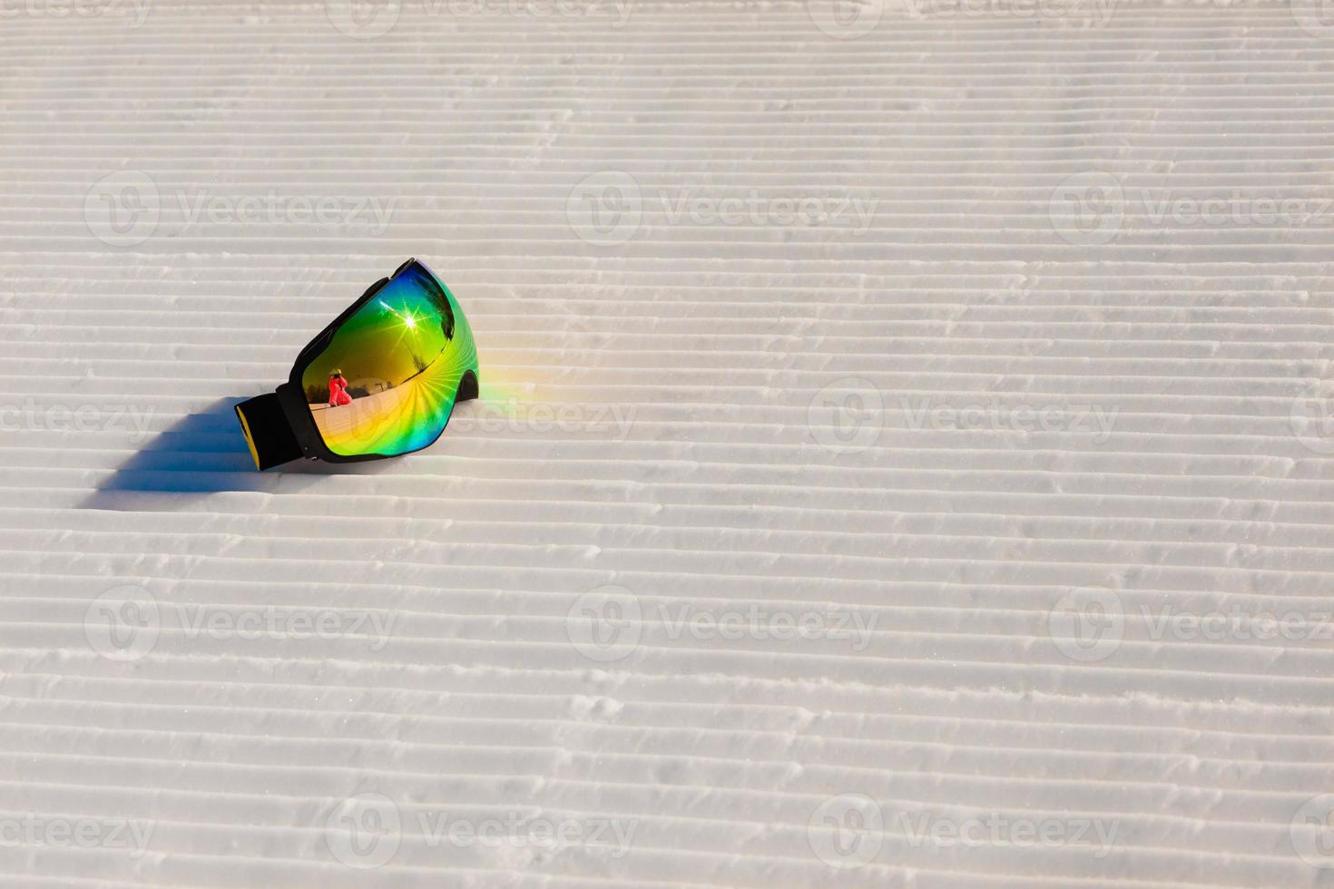 Skibrille, die auf einem neuen präparierten Schnee und einer leeren Skipiste liegt foto