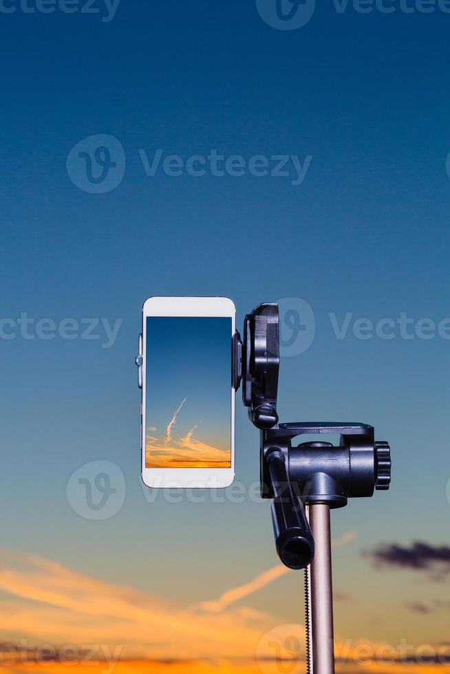 Smartphone auf Stativ zur Aufnahme des Sonnenuntergangs im vertikalen Modus foto