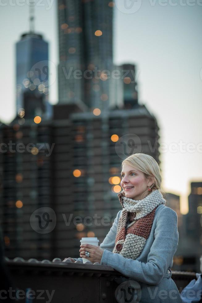 Frau auf der Brooklyn Bridge, die Manhattan mit einem Kaffee betrachtet foto
