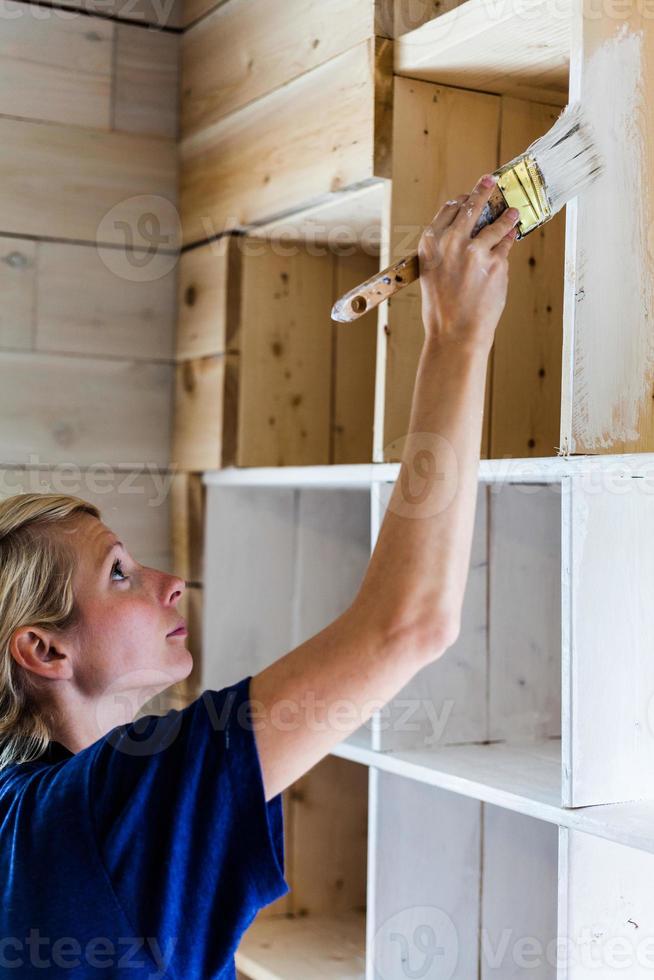 Frau trägt die erste Farbschicht auf einer Holzbibliothek auf foto