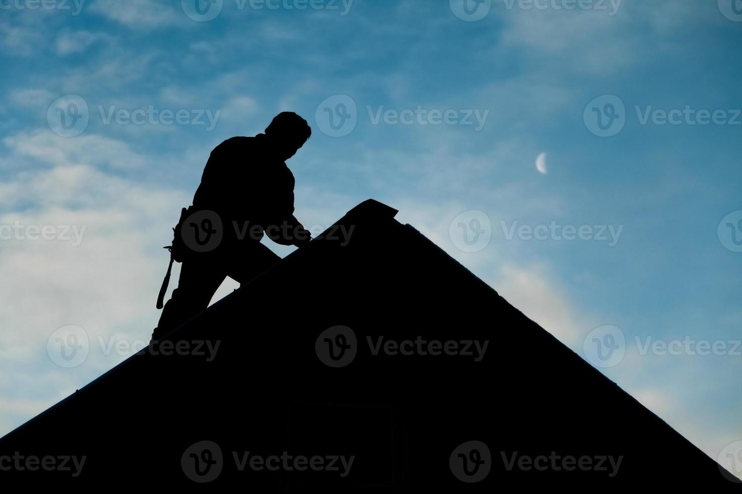 Auftragnehmer in Silhouette, der auf einem Dach arbeitet foto