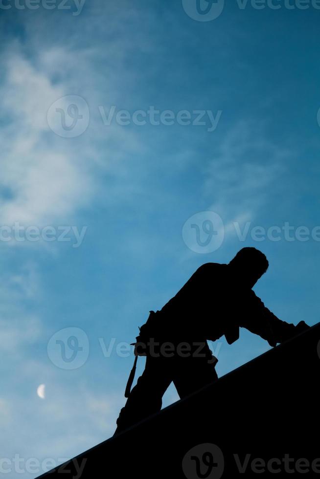 Auftragnehmer in Silhouette, der auf einem Dach arbeitet foto