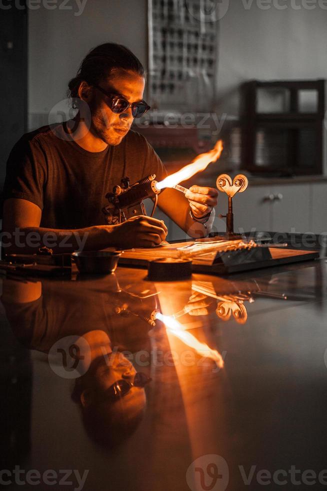 Glasbläser junger Mann, der an einer Fackelflamme mit Glasröhren arbeitet foto