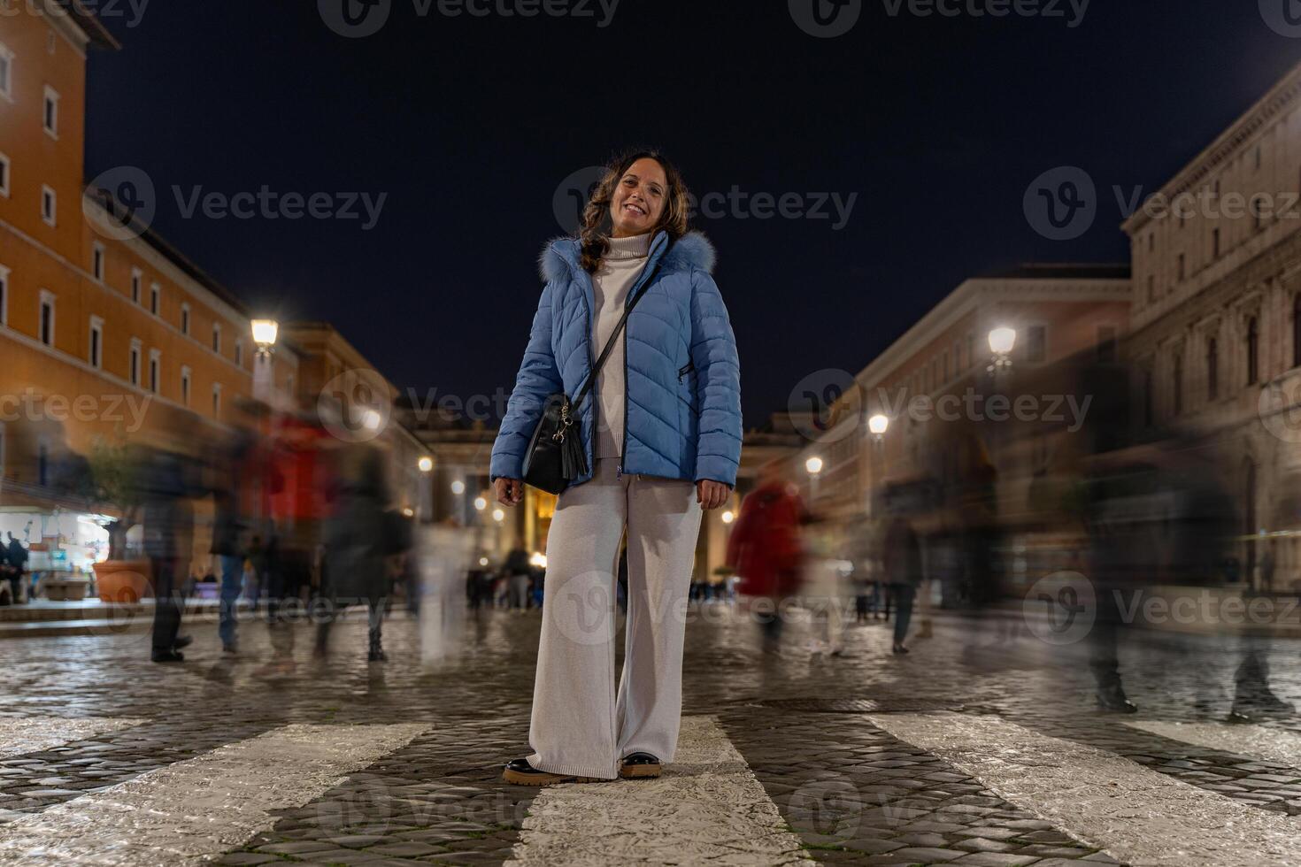 weiblich Tourist posieren unter verschwommen Menschen Gehen beim Nacht auf ein Straße im Vorderseite von das Vatikan im Rom foto