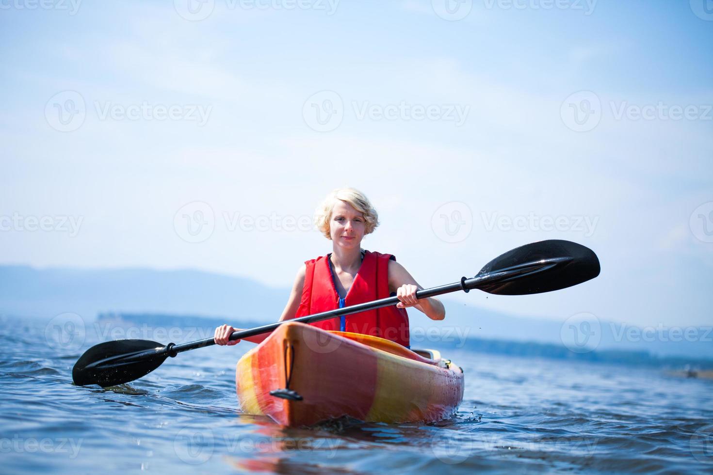 Frau mit Sicherheitsweste, die allein auf einer ruhigen See Kajak fährt foto